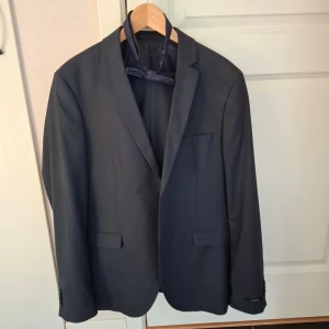 Mörkblå kavaj och byxa med fluga från Jack & Jones - Säljer en stilren mörkblå kavaj från Jack & Jones Premium, storlek 52 (herr L). Byxor storlek 50. Kavajen har slim stretch passform, två fickor med lock och medföljande blå fluga med diskret mönster. Perfekt för bal eller fest.