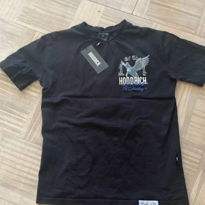 Svart t-shirt från Hoodrich med Pegasus-tryck - Säljer en svart t-shirt från Hoodrich i storlek M med Pegasus-tryck och texten 'Product of the Streets' på ryggen. Framtill finns ett mindre tryck med logga och motiv. Klassisk passform och rund halsringning.