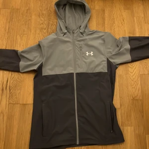 Grå och svart vindjacka från Under Armour - Jätte fin Under armour jacka som jag köpte från Jd sports. Matchar med allt och jag har fått jätte många komplimanger från den.