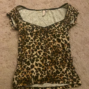 Leopardmönstrad topp från Nelly - Säljer en snygg leopardmönstrad topp från Nelly i storlek XXS. Toppen har korta ärmar, v-ringad hals och är figurnära. Perfekt för dig som gillar djurmönster och vill sticka ut lite extra.