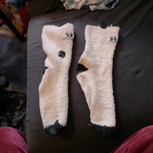 Vita fluffiga strumpor med kattmotiv - Supermjuka och mysiga vita strumpor med svart kattansikte och svarta detaljer på tår och häl. Strumporna har ett gulligt broderat kattansikte framtill och svarta fläckar som påminner om en katt.st 36-48