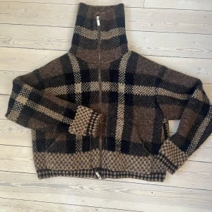 Brun och svart rutig ulljacka från Zara - Säljer en brun och svart rutig jacka från Zara med hög krage och dragkedja framtill. Jackan är i ullmaterial och har långa ärmar samt en oversized passform. Perfekt för kyliga dagar.