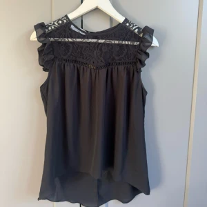 Svart blus med spets från Rinascimento - Supersnygg svart blus från Rinascimento med spetsdetaljer upptill och volang vid axlarna. Köpt från Sellpy men aldirg använt