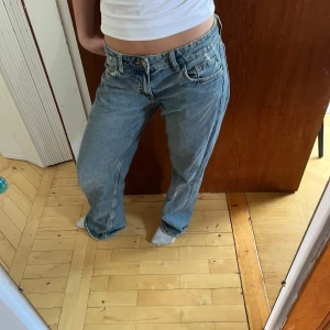 Ljusblå raka jeans från Zara  - Säljer ett par klassiska ljusblå jeans från zara med rak passform och låg midja. Jeansen har fem fickor, knappgylf och är i ett mjukt denimtyg. Perfekta för en avslappnad stil.