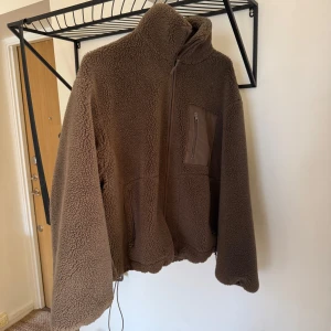 Brun teddyjacka från & Other Stories - Mysig brun teddyjacka från & Other Stories med hög krage och dragkedja framtill. Jackan har en bröstficka med dragkedja och två fickor.
