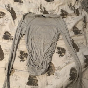 Ljusgrå långärmad topp från H&M Divided - Säljer en ljusgrå långärmad topp från H&M Divided. Toppen har en tight passform och rynkade detaljer på ena sidan vilket ger en snygg effekt. Perfekt att styla med jeans eller kjol.