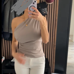 Beige oneshoulder topp från Zara - Säljer en beige oneshoulder topp med tight passform. Toppen är från Zara och har en stilren  look med draperad effekt över bysten. Storlek S
