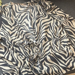 Zebramönstrad blus från ONLY - Säljer en snygg zebramönstrad blus från ONLY med v-ringning och knytning i midjan. Klänningen har svart och beige mönster och är perfekt för dig som vill ha en snygg blus Superskön. Oanvänd 