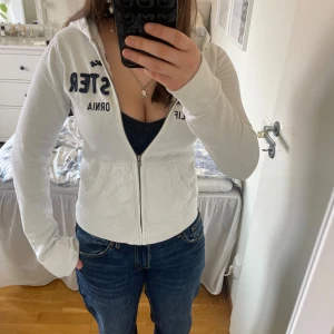 Vit zip-hoodie från Hollister - Vit hoodie med dragkedja från Hollister. Broderad marinblå text på bröstet och fickor framtill. Mjuk bomullskänsla och huva. Perfekt för en avslappnad stil. Storlek S💕pris går att pruta ner❣️