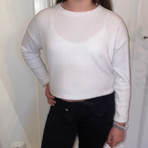 Vit ribbad tröja från H&M - Säljer en vit ribbad långärmad tröja från H&M. Tröjan har en rund halsringning och är något croppad i modellen. Perfekt för en enkel och stilren look.