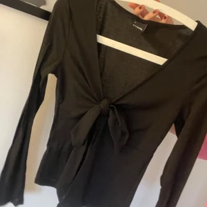 Svart långärmad topp med knyt från Gina Tricot - Säljer en svart långärmad topp från Gina Tricot med v-ringning och snygg knytning framtill. Perfelt tröja till sommaren. Säljer pga att jag inte använder den. 