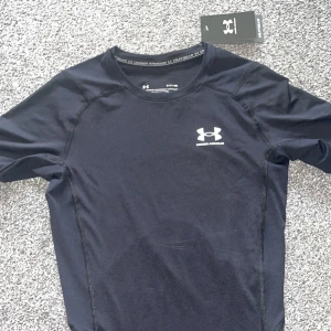 Svart kompressionströja från Under Armour - Säljer en svart kompressionströja från Under Armour med HeatGear-teknologi. Tröjan är helt ny med tags och oanvänd. Sitter perfekt och tight vid armarna och resten av överkroppen 💪