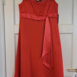 Helt ny! Korallröd festklänning Medium/40 - Säljer en korallröd knälång klänning från Vera Mont med vackert tyg med fin lyster och fint fall, satinmidjedetalj och knytband. Helt ny med prislapp kvar, nypris 1698kr. Perfekt för sommarens festligheter.