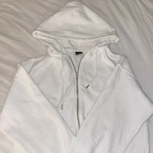 Vit hoodie med dragkedja från Gina Tricot - Säljer en klassisk vit hoodie från Gina Tricot i storlek XS. Tröjan har dragkedja framtill, huva med snören och ribbade muddar. Knappt använd.