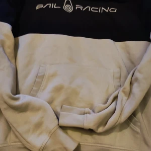 Tvåfärgad hoodie från Sail Racing - Säljer en snygg hoodie från Sail Racing i storlek S. Tröjan är tvåfärgad med svart upptill och ljusbeige nedtill, har magficka och tryckt logga på bröstet. Perfekt för en avslappnad stil och sköna dagar. Även fler tröjor från Sail Racing stl S 135kr/st eller paketpris alla för 280 kr