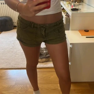 Olivgröna shorts - Snygga olivgröna line shorts med låg midja och knappdetaljer. Perfekta för varma sommardagar. De har en tight passform och är tillverkade i ett bekvämt material. Dom är andvända 1 gång för fel storlek. Fråga om mer bilder eller mått om ni vill (Lånade bilder)