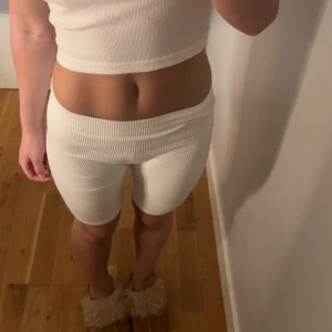 Vita ribbade cykelshorts - Säljer ett par vita ribbade cykelshorts med midwaist passform. De är stretchiga och sitter tight, perfekta för en sportig look eller chill hemma. Materialet är mjukt och bekvämt, passar perfekt till sommarens varma dagar.