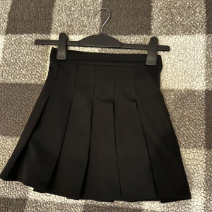Svart plisserad kjol XXS - Snygg svart kortkjol från FB Sister i plisserad modell. Kjolen har dragkedja bak och är tillverkad i ett mjukt, lätt material som ger en clean och stilren look. Perfekt för dig som gillar klassisk och enkel stil. Sällan använd