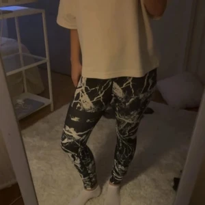 Svarta Stronger leggings med marmorprint - Säljer ett par svarta leggings från Stronger med vitt marmorprint. De har hög midja och elastisk linning med logga. Sitter tight och är perfekta för träning eller chill. Materialet är stretchigt och bekvämt syntet.