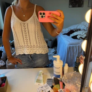 Vit stickad linnetopp med spetsdetaljer - Superfin vit stickad linnetopp med smala axelband och v-ringning. Toppen har ett snyggt hålmönster och spetsinspirerade detaljer längs nederkanten. Perfekt för varma dagar och ger en söt, bohemisk vibe.