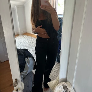 Svarta bootcut byxor med medel midja - Säljer ett par svarta byxor med bootcut och hög midja. De har klassisk femficksdesign och raka ben som blir vidare nertill. Snygga till crop top eller hoodie och passar perfekt om du gillar en clean och stilren look.