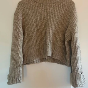 Beige stickad tröja från Gina Tricot - Mysig beige stickad tröja från Gina Tricot i storlek XS. Tröjan har grov ribbstickning, lång ärm med uppvik och en något croppad passform. Perfekt för lager-på-lager och chill höst- och vinterstil.