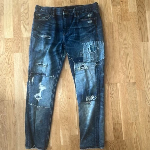 Polo ralph lauren jeans  - Säljer ett par mörkblå jeans från polo Ralph lauren med coola slitningar och patchade detaljer på benen. Dessa jeans är väldigt sällsynta då de inte tillverkas längre och finns bara få av dom. Jeansen är storlek 31 men jag har kortat ner dom till cirka 88 cm men midjan är samma. Använd 1 gång