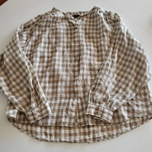 Rutig linneskjorta från Massimo Dutti - Beige och vit rutig skjorta från Massimo Dutti i luftig linne. Skjortan har lång ärm, knappar framtill och klassisk krage. Perfekt för en avslappnad och stilren look.