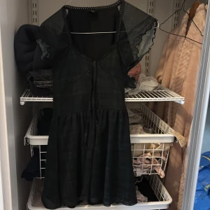 Svartgrön rutig klänning / playsuit från Urban Outfitters - Supersöt kort klänning / playsuit från Urban i svart och mörkgrön rutig design. Klänningen har meshärmar, v-ringning med spetskant och snörning framtill. 