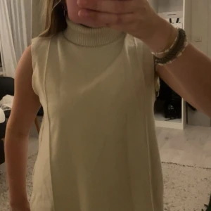 Beige stickad  topp från Zara - Säljer en beige stickad väst från Zara med hög polokrage. Västen är ärmlös och har en rak, loose passform som ger en chill vibe. Perfekt att styla över en skjorta eller t-shirt för en trendig lager-på-lager-look.