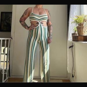 Randig stickad byxdress med cut out - byxdress med gröna, vita, orange och gula ränder. Byxdressen har smala axelband, cut out-detalj framtill och vida ben. Materialet är stickat och känns mjukt mot huden. 