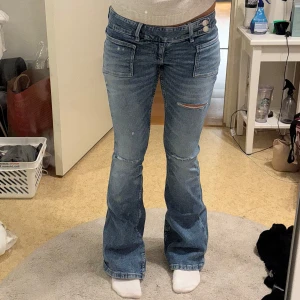 Blå bootcut jeans med slitningar - Snygga blå bootcut jeans med låg midja och slitningar på låret samt fransiga benslut. Perfekta för en avslappnad och trendig look. Lite slitna vid bensluten men inget man tänker på 🥰Ensast använda ett fåtal gånger. Innerbenslängd: 82 cm och midjemått: 37 cm
