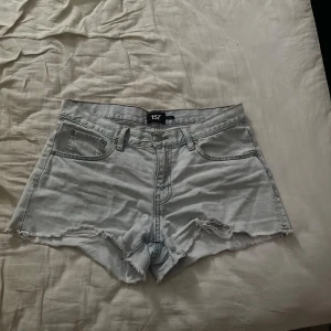 Ljusblå jeansshorts från 157 - Snygga ljusblå jeansshorts från 157 med hög midja och råa, fransiga kanter. Klassisk femficksmodell med dragkedja och knapp framtill. Perfekta för varma dagar och ger en avslappnad vibe. Storlek M