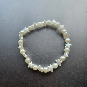 Pärlarmband med stjärnor i vitt - Supergulligt armband med vita pärlor och stjärnformade detaljer. Stretchig modell som passar de flesta handleder. Perfekt accessoar för att ge din outfit en söt och lekfull touch.