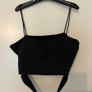 Svart croppad topp från SHEIN - Svart croppad topp från SHEIN med tunna axelband och knytband nedtill. Material är både mjukt och lätt, vilket gör den bekväm att bära under exempelvis varma dagar ✨✨