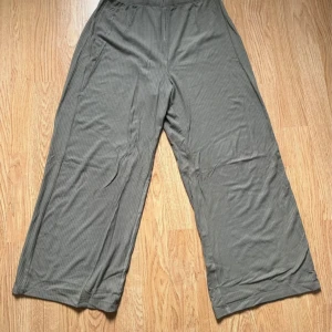 Olivgrön pull-on byxa - Snygga olivgröna byxor med ribbad struktur och bred passform. De har hög midja och croppad längd, vilket ger en chill och trendig vibe. Perfekta för dig som gillar bekväma men stilrena plagg