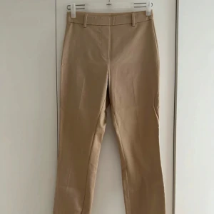 Beige byxa - Snygga beiga byxor från H&Mmed klassisk rak passform. Byxorna har hällor för bälte, två bakfickor och är tillverkade i ett mjukt bomullsmaterial med lite glans. Perfekta för en clean och stilren look. Byxan har ingen dragkedja