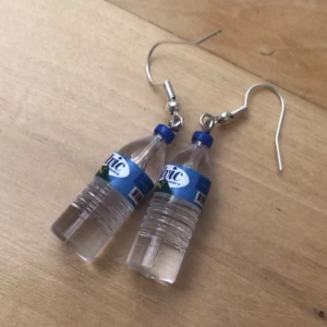 Örhängen med vattenflaskor - Unika örhängen formade som små vattenflaskor med blå etikett och lock. Perfekt för dig som gillar roliga och annorlunda accessoarer. Hängande modell med silvriga krokar. Ger en lekfull och kreativ touch till din stil. Priset gäller för ett par (de i bilden) men det finns 5 par i lager (de i bilden är inkluderade) så man kan köa alla 5 paren för 30kr💞