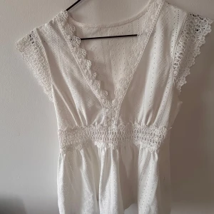 Vit spetsblus med v-ringning - Superfin vit blus med v-ringning och spetsdetaljer längs kanterna. Blusen har broderade mönster, smock i midjan och är ärmlös med volangkant. Annonsen finns på flera ställen så skriv till mig innan ni trycker på köp🫶🏻