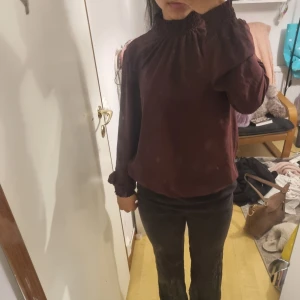 Mörklila blus med hög krage - Säljer en mörklila blus med långärmade puffärmar och smockad hög krage. Blusen har även smockade ärmslut som ger en snygg detalj. Perfekt att styla med jeans eller kjol för en trendig look.