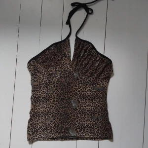 Leopardmönstrad halterneck topp - Snygg halterneck topp i leopardmönstrat tyg med fjärilar. Toppen har knyt i nacken, v-ringning och svarta kantband. Perfekt för dig som vill sticka ut med ett djurmönster och unika detaljer. Storlek S-M.