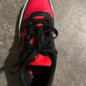 Nike Jordan 1 Low röd/svart EUR 36 - Snygga Nike Jordan 1 Low sneakers i rött och svart skinn med klassisk vit mellansula och röd yttersula. Skorna har svart snörning, rund tå och ikonisk Swoosh på sidan. Perfekta för dig som vill sticka ut med en tidlös streetstyle.