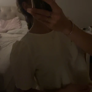 Vit blus med puffärm  - Säljer en söt vit blus med puffiga korta ärmar och rund halsringning. Blusen har en pärldetalj vid halsen och är gjord i ett strukturerat tyg som ger en lyxig känsla. Perfekt för dig som gillar stilrena och feminina plagg.