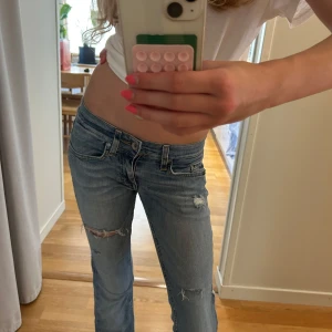 Ljusblå bootcut jeans med slitningar - Säljer ett par ljusblå jeans med bootcut passform och snygga slitningar på benen. Jeansen har låg midja och är tillverkade i mjukt denim. Perfekta för dig som gillar en avslappnad och trendig look. Säljer då dem tyvärr är för korta för mig. Jag har vanligtvis w25 och de sitter bra i midjan ❤️skriv vid funderingar angående mått mm.