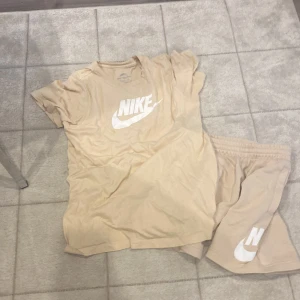 Beige Nike t-shirt med logga - Snygg beige t-shirt från Nike med stor vit logga framtill. Klassisk passform och korta ärmar, perfekt till chill eller träning. Tillverkad i mjuk bomull som känns skön mot huden. Enkel och stilren design som funkar till det mesta.
