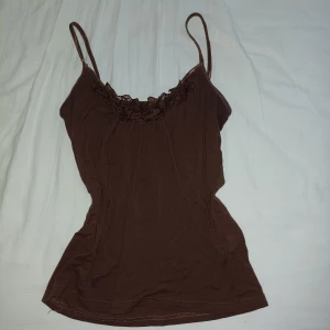 Brun linnetopp - Säljer en brun linnetopp med smala axelband och snygg blom-design med pärlor högst upp. Toppen har en figurnära passform och är perfekt för dig som gillar en enkel men ändå söt stil.