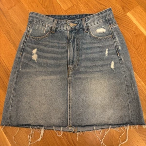 Blå jeanskjol med slitningar från H&M - Snygg blå högmidjad jeanskjol från H&M . Kjolen har aldrig använts därav inga skador💓Köparen står för frakten