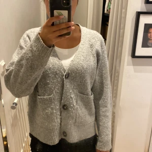 Grå kofta från Vero Moda - Mysig grå kofta från Vero Moda med stora knappar framtill och två fickor. 