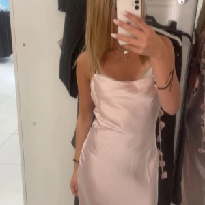 Ljusrosa långklänning i satin - Supersnygg ljusrosa långklänning i satin med smala axelband och dekorativa blommor längs sidan. Klänningen har en elegant, slät siluett och lätt draperad urringning. Perfekt för dig som vill sticka ut med en romantisk vibe.  använd en gång på lärarmiddag, kom privat angående frågor❤️sitter lite långt på mig som e 164