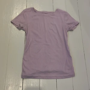 Ljuslila ribbad t-shirt FSBN Sister - Supersöt ljuslila t-shirt från FSBN Sister i ribbad bomull. Modellen är kortärmad med rund halsringning och har en slim passform som sitter snyggt. Perfekt att matcha med jeans eller kjol för en chill men samtidigt snygg look.